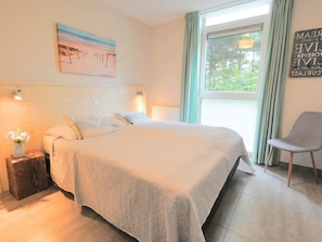 A bedroom with a bed, a window with curtains, a chair, and a wall with a painting. - Holiday Home With 3 Bedrooms (Sint Maartensvlotbrug)
