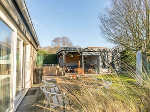 A patio with metal chairs, a wooden table, and a covered seating area with cushions and a table. - Holiday Home in Renesse With Swimming Pool (Renesse)