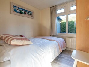 A bedroom with a bed, a window with curtains, a radiator, and a painting on the wall. - Holiday Home in Renesse With Swimming Pool (Renesse)