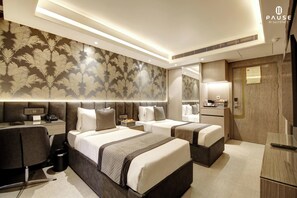 Ein Hotelzimmer mit zwei Betten, einem Schreibtisch, einem Stuhl, einer Mülleimer und einem Spiegel.