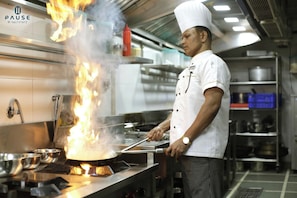 Un chef cocina con llamas sobre una estufa en una cocina profesional.