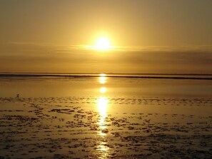 Ein Strand bei Sonnenuntergang mit ruhiger See und blauem Himmel.