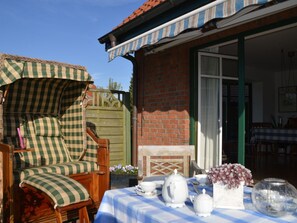 A patio with a checkered umbrella, a table set with white teapots and cups, and a brick wall. - Holiday Apartment With 2 Bedrooms (Barkelsby)