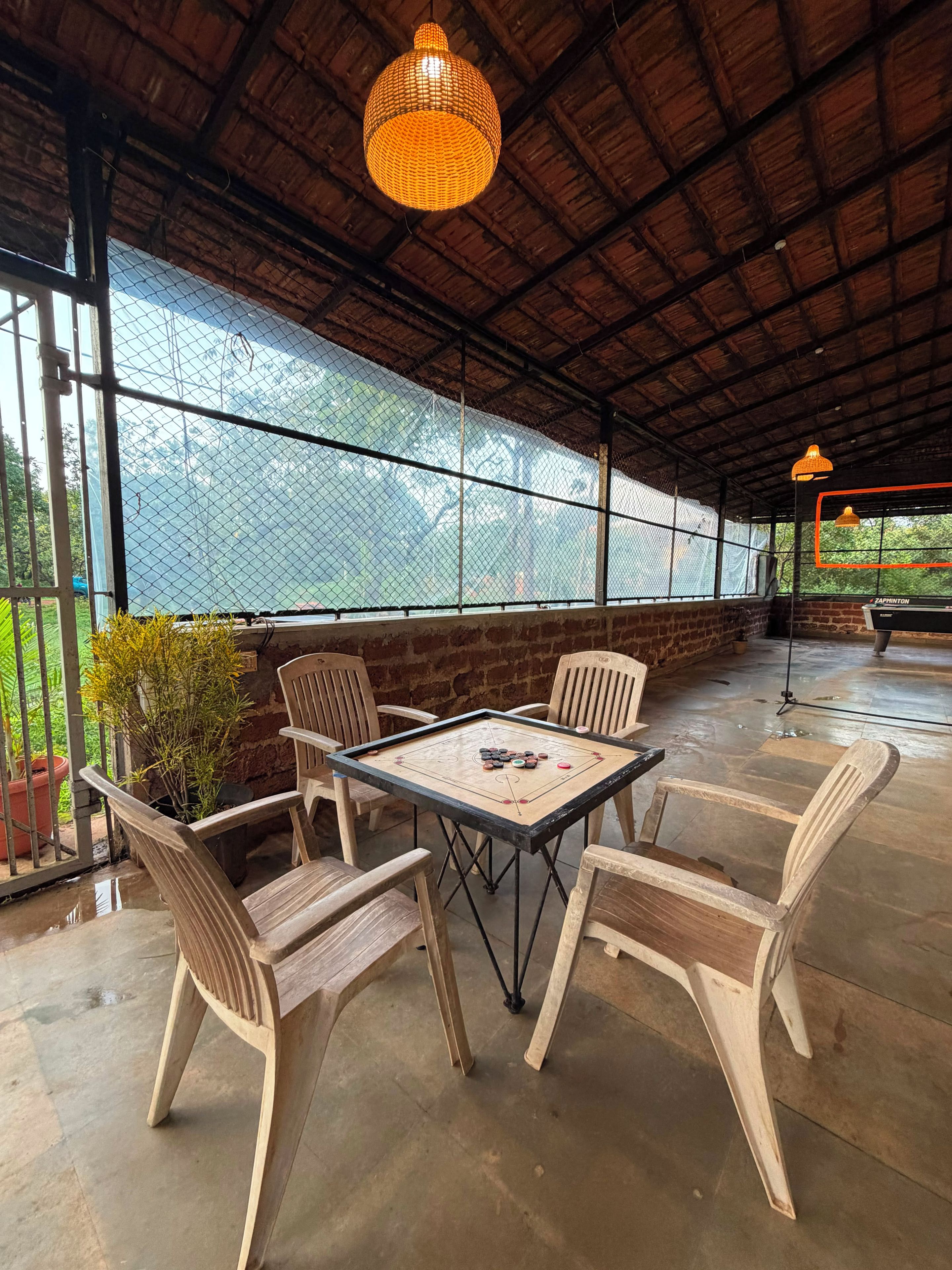 Un área de estar al aire libre con una mesa y sillas, un colgante de luz y una vista a través de una malla.