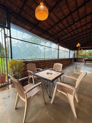 An outdoor seating area with a table and chairs, a hanging light fixture, and a view through a mesh screen. - The Sonchafa Farmstay (Sangameshwar)