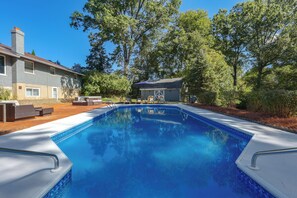 Una piscina con superficie de agua azul cristalina, rodeada por una zona de patio con mobiliario exterior.