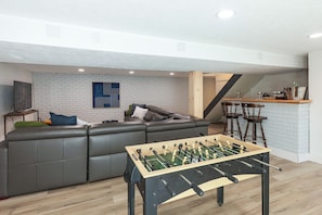 Ein modernes Wohnzimmer mit einem Ecksofa, einem Kicker und einer Ziegelwand.