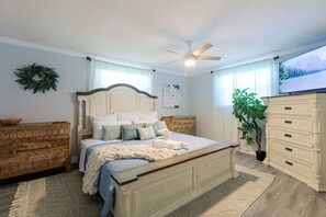 Un dormitorio con cama, cómoda, ventilador de techo, televisor y una planta.