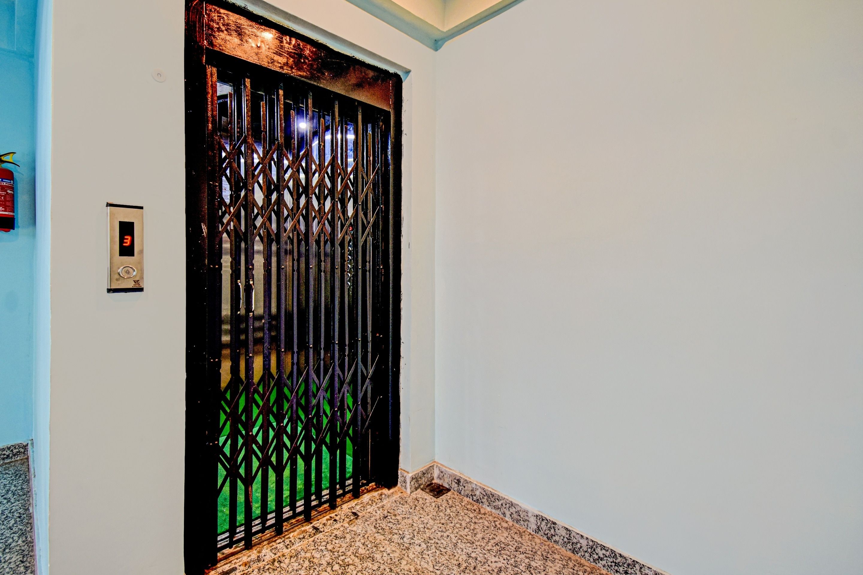 Una puerta con reja de seguridad, detector de incendios y suelo de mármol.