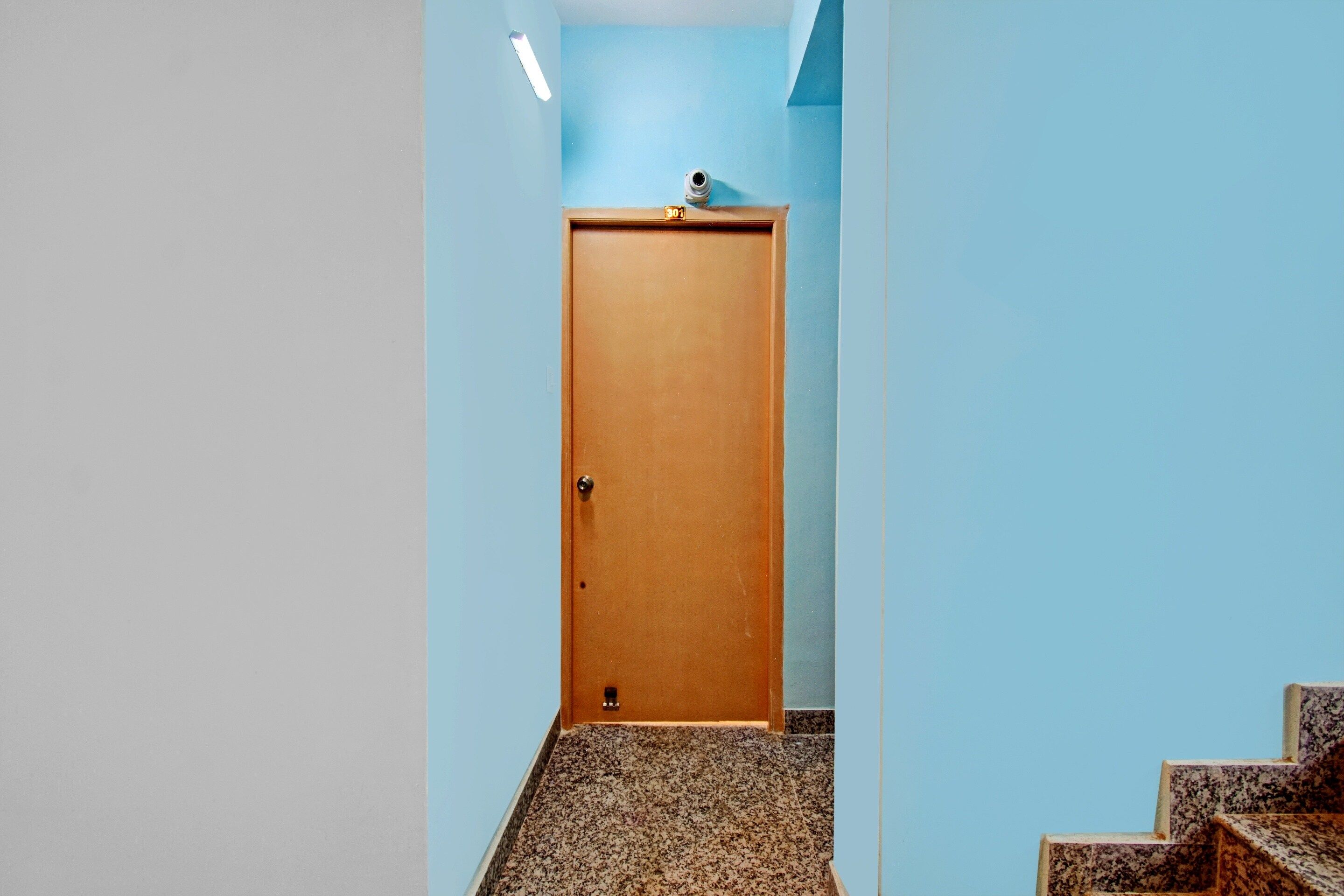 A hallway with a wooden door, light blue walls, and a granite floor.