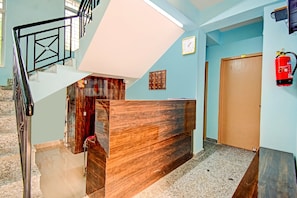 Un vestíbulo de hotel con una recepción, una escalera, un extintor y una puerta.