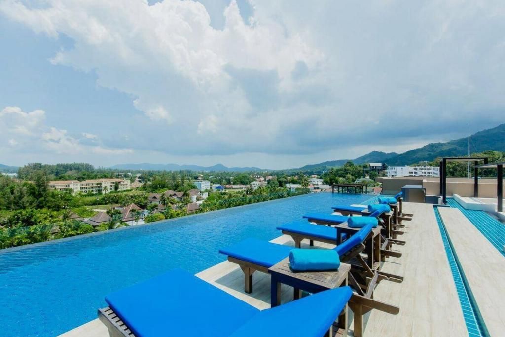 Una piscina infinita en la azotea, con sillones azules y vistas a una zona turística.