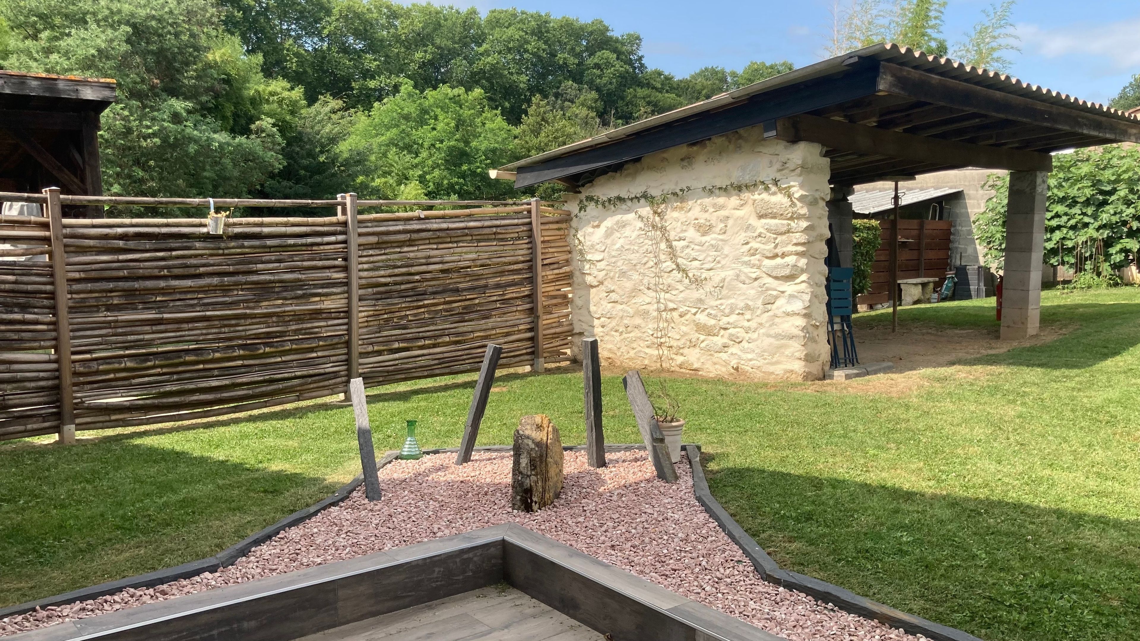Un área exterior vallada con una estructura de piedra, un banco de madera y un pequeño jardín con piedras.