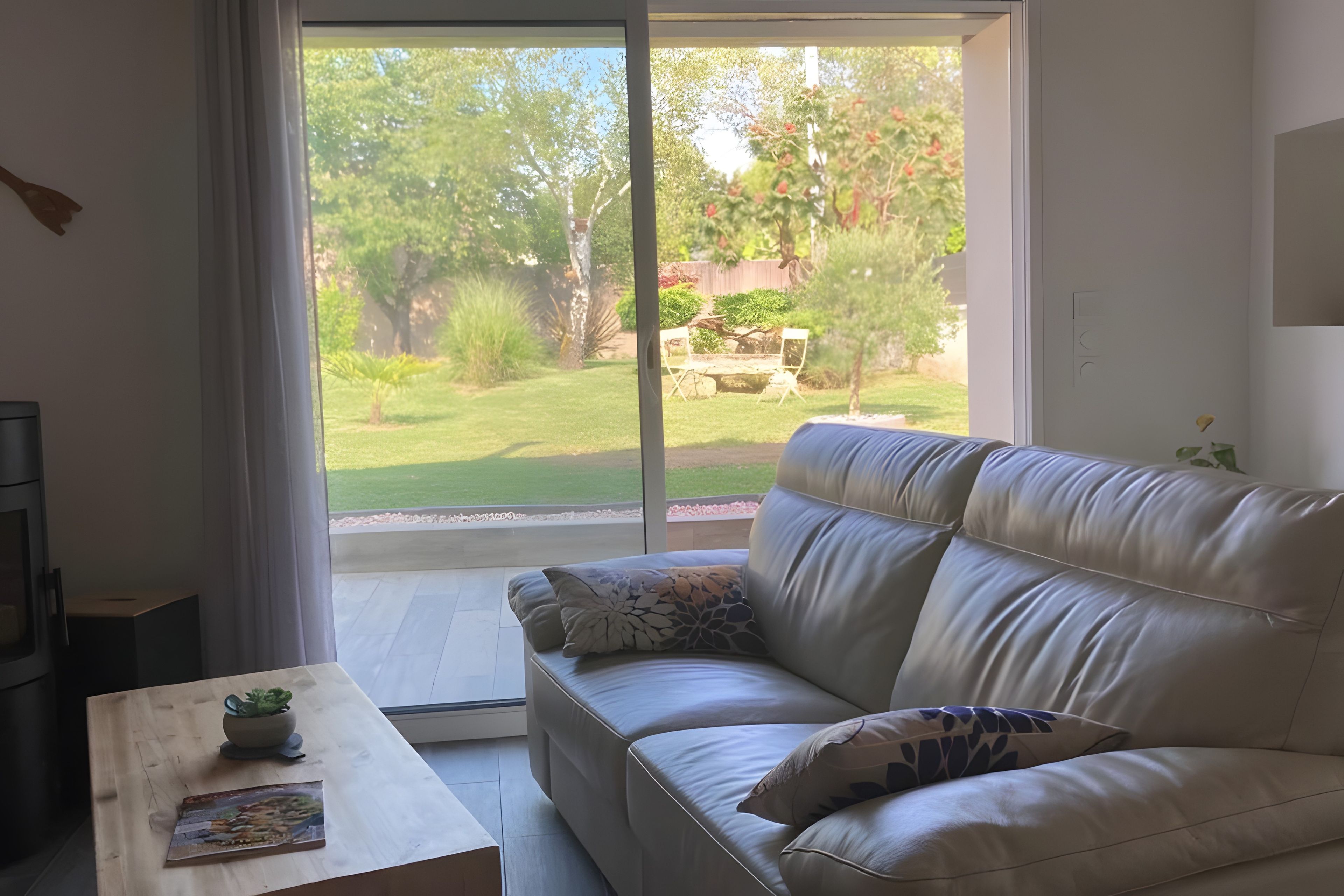 A modern living room with a sofa, a coffee table, and a view of a garden through a large window.