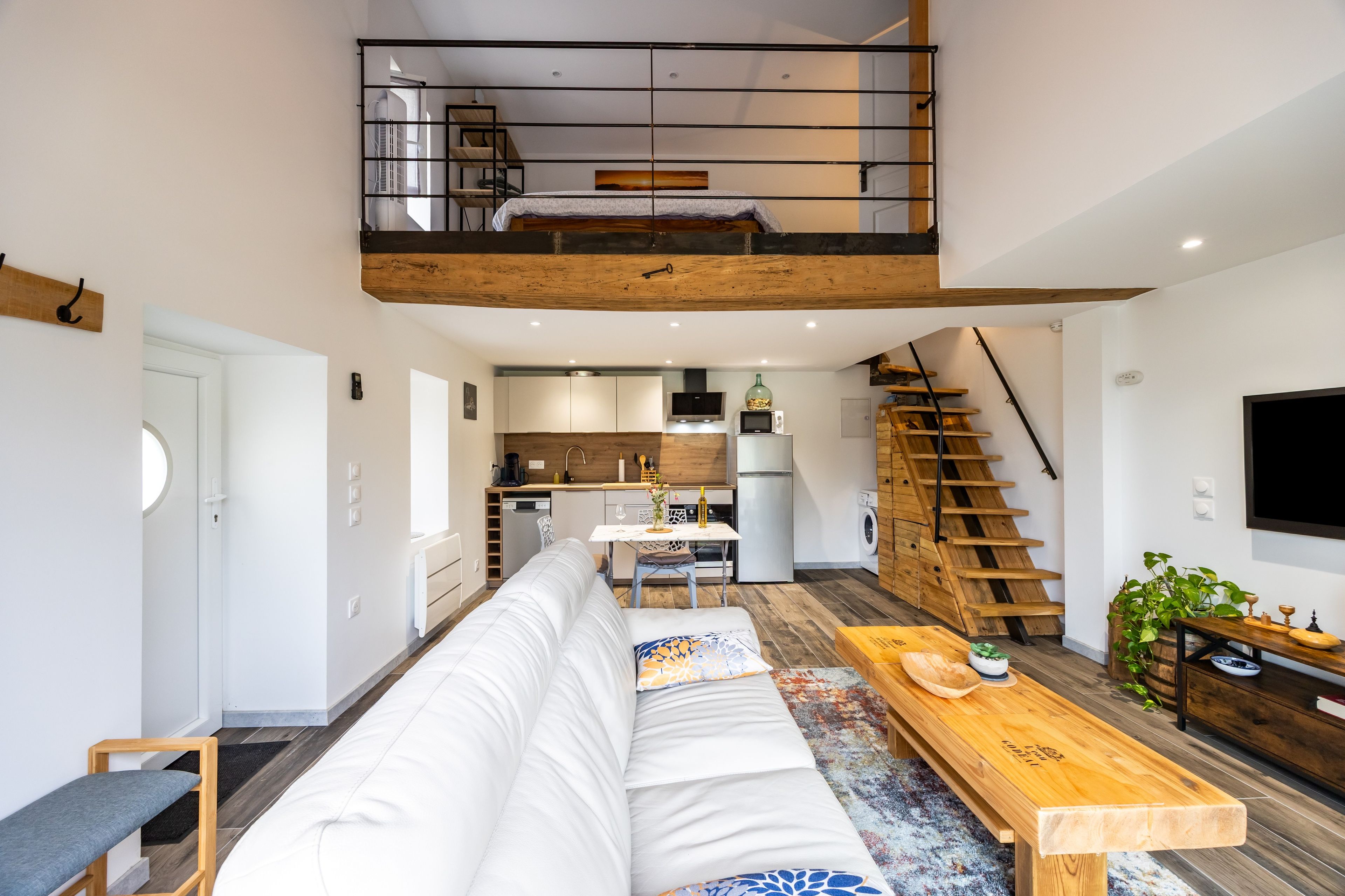 Un apartamento moderno estilo loft con cama en altillo, cocina, comedor y escalera.