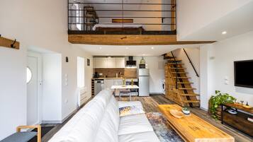 Un apartamento moderno estilo loft con cama en altillo, cocina, comedor y escalera.