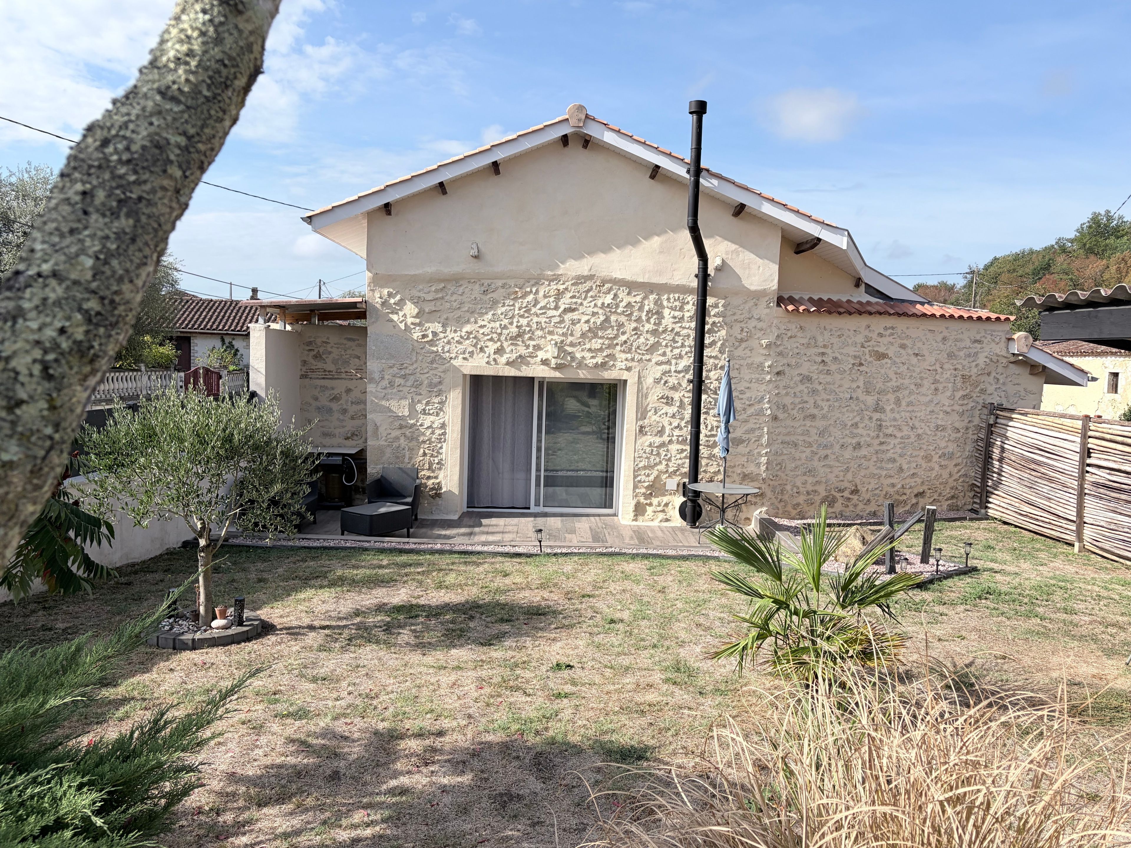 Una casa de piedra con techo de tejas, un patio con mobiliario exterior y un pequeño jardín.