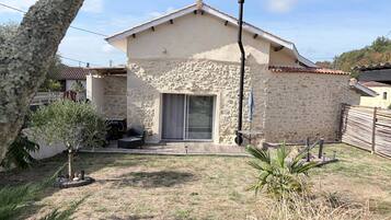 Una casa de piedra con techo de tejas, un patio con mobiliario exterior y un pequeño jardín.