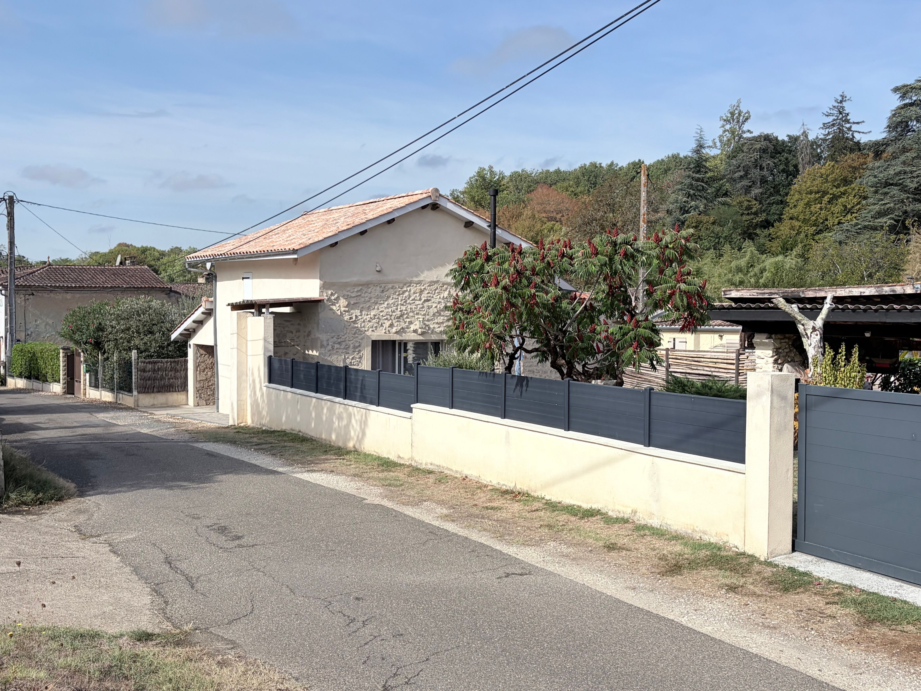 A residential property with a stone facade, a tiled roof, and a fenced yard.