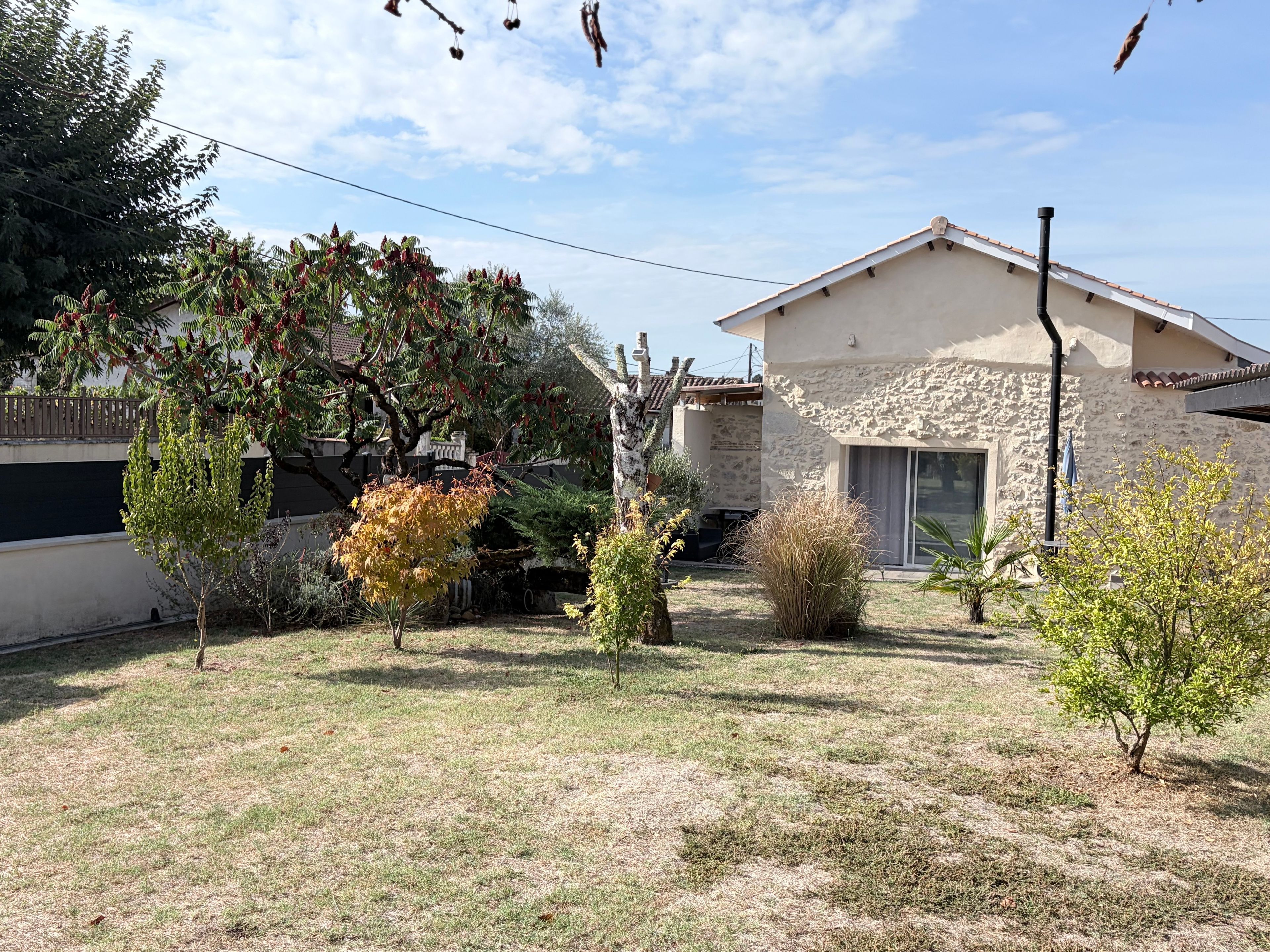 A stone house with a sloped roof, a small garden with various plants, and a clear sky.