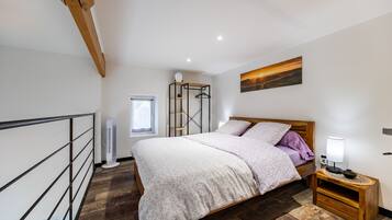 Un dormitorio con cama, mesita de noche, ventana, radiador y un cuadro en la pared.