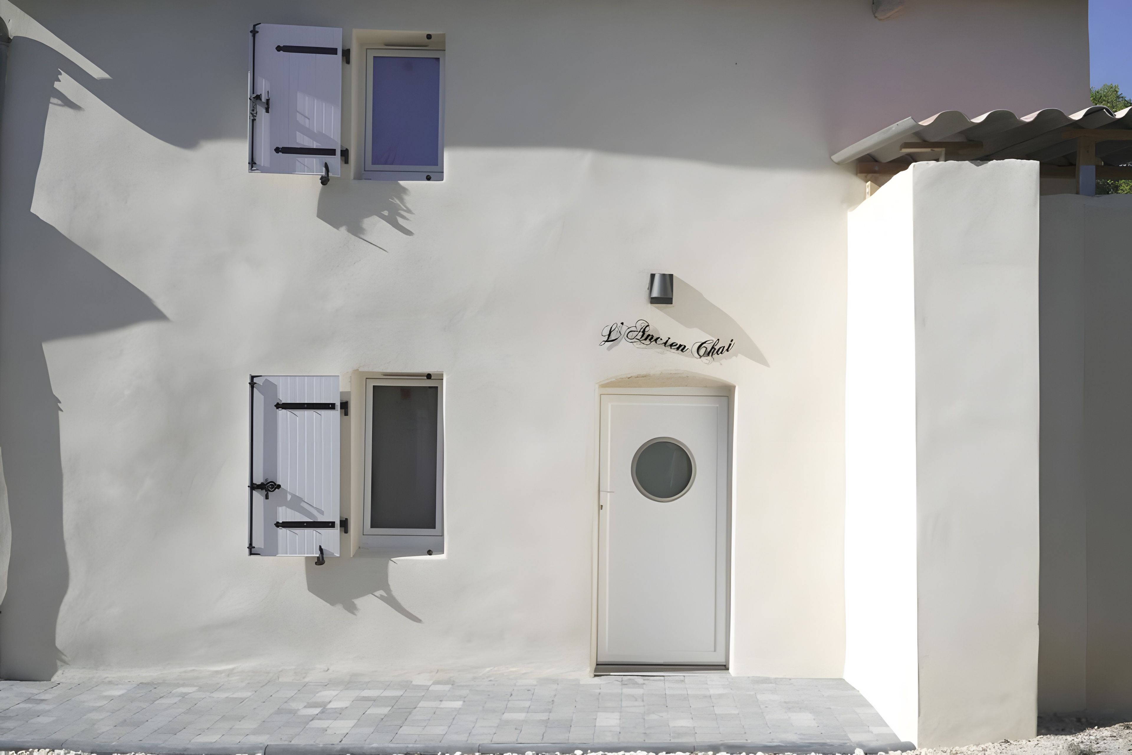 A building facade with a white exterior, a door with a circular window, and two windows with shutters.
