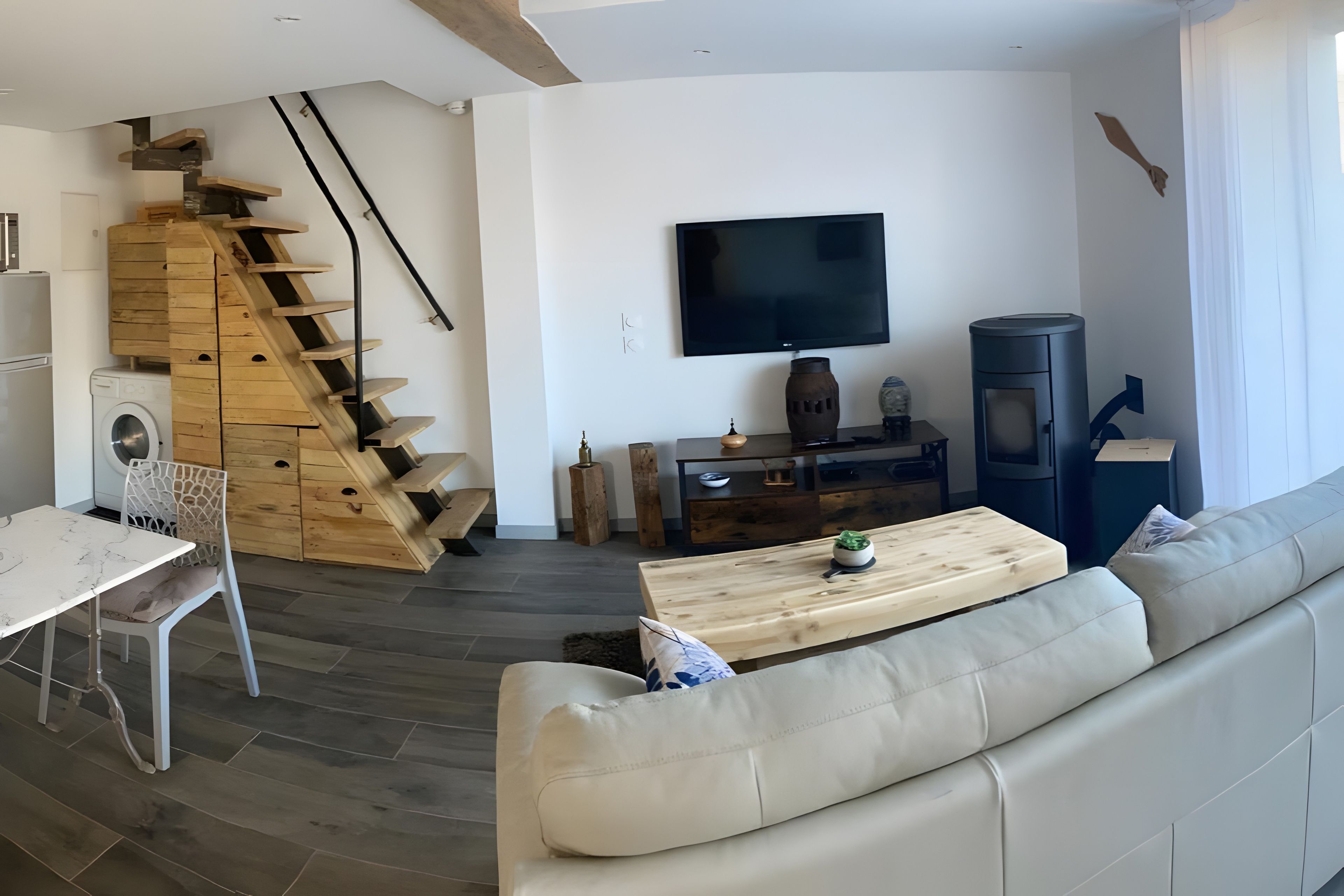 A modern living room with a sofa, a wooden staircase, a flat-screen TV, and a small table.