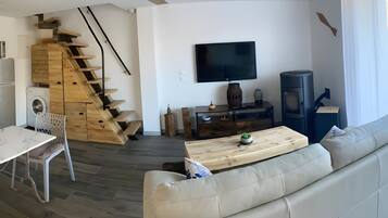 A modern living room with a sofa, a wooden staircase, a flat-screen TV, and a small table.