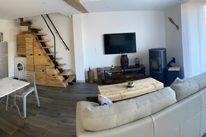 A modern living room with a sofa, a wooden staircase, a flat-screen TV, and a small table.