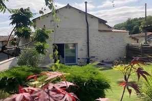 Ein Haus mit Steinaußenwand, einer Tür und einer kleinen Terrasse mit Stühlen.