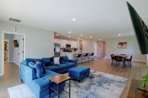 Un salon moderne avec un canapé d’angle, une table basse et un coin repas comprenant une table et des chaises en bois.