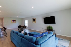 A modern living room with a sectional sofa, dining table, chairs, and a flat-screen TV mounted on the wall. - 12 Mi to Disney! Family Home ChampionsGate Golf (Davenport)