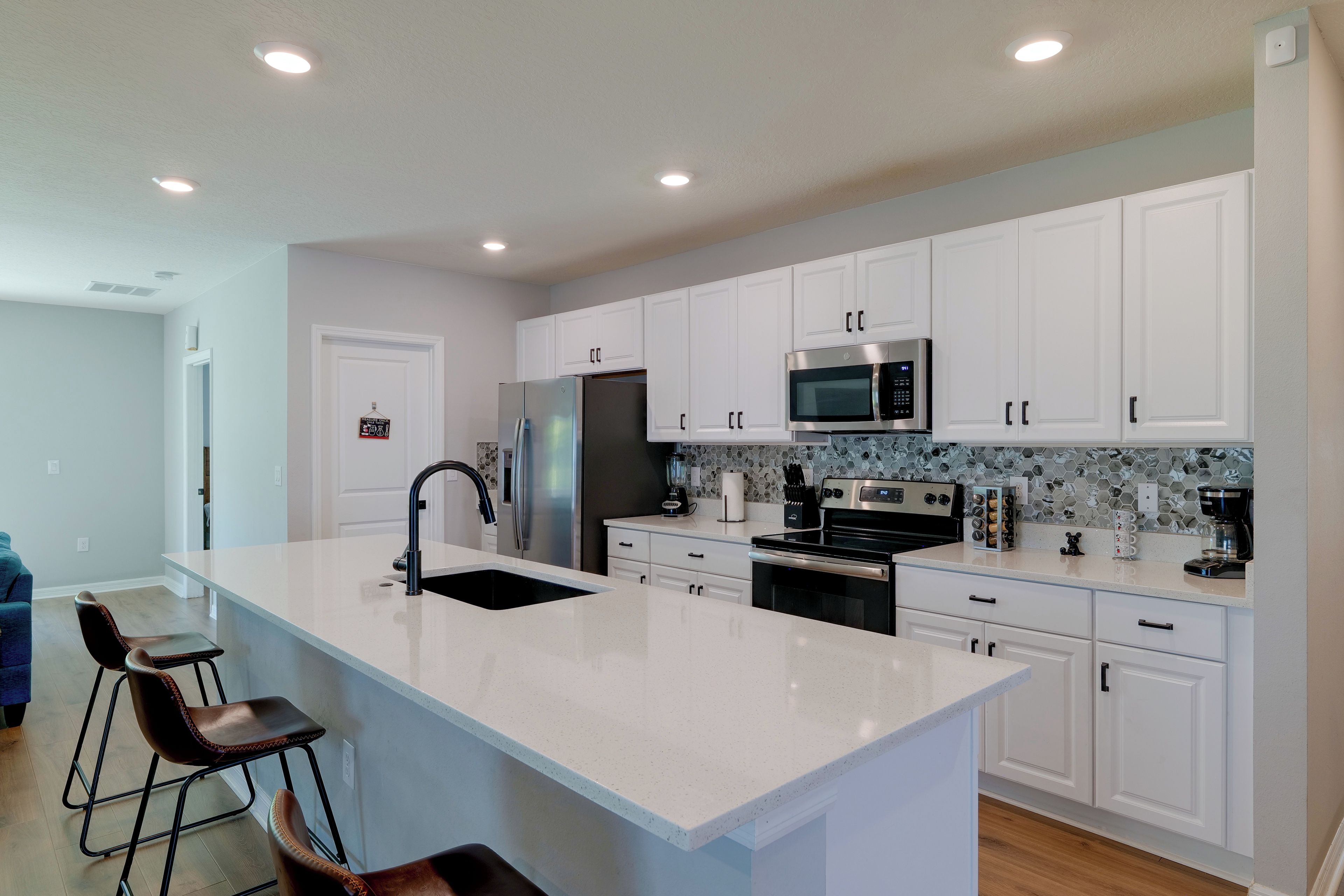 A modern kitchen with white cabinets, stainless steel appliances, a large island with bar stools, and a tiled backsplash.