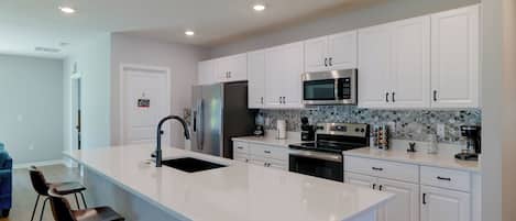 Una cocina moderna con armarios blancos, electrodomésticos de acero inoxidable, una isla grande con taburetes y un salpicadero de azulejos.