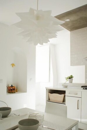 A modern kitchen with white cabinetry, a hanging paper flower chandelier, and a small potted plant on the counter. - Casa de Baixo in Coimbra (Coimbra)