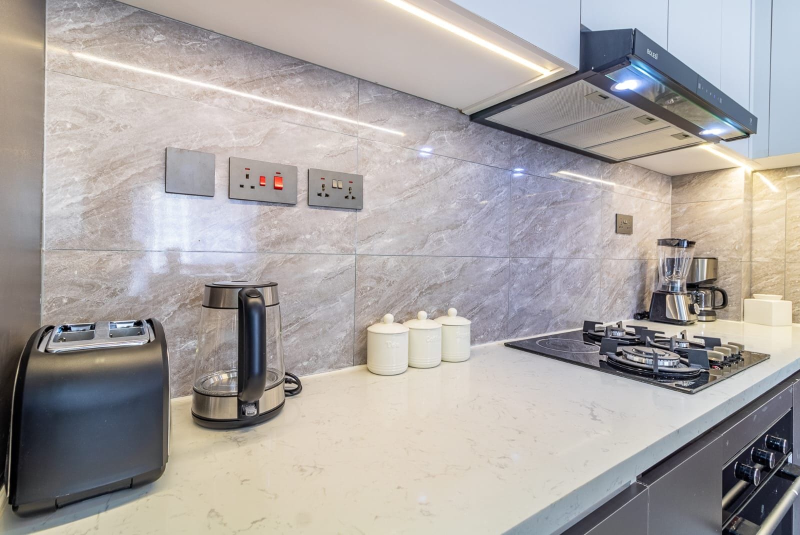 A modern kitchen with a marble backsplash, a coffee maker, a toaster, and a stove.