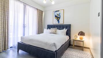 Une chambre à coucher moderne avec un grand lit, une table de chevet avec une lampe et un tableau au mur.