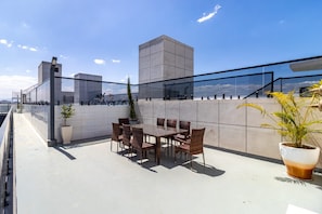 Een dakterras met een tafel en stoelen, plantenbakken en uitzicht over de stad.