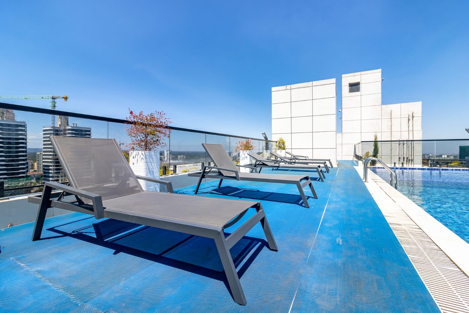 Un área de piscina en la azotea con sillones de descanso y una vista despejada del horizonte de la ciudad.