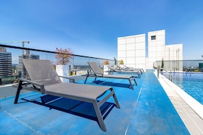 Un área de piscina en la azotea con sillones de descanso y una vista despejada del horizonte de la ciudad.