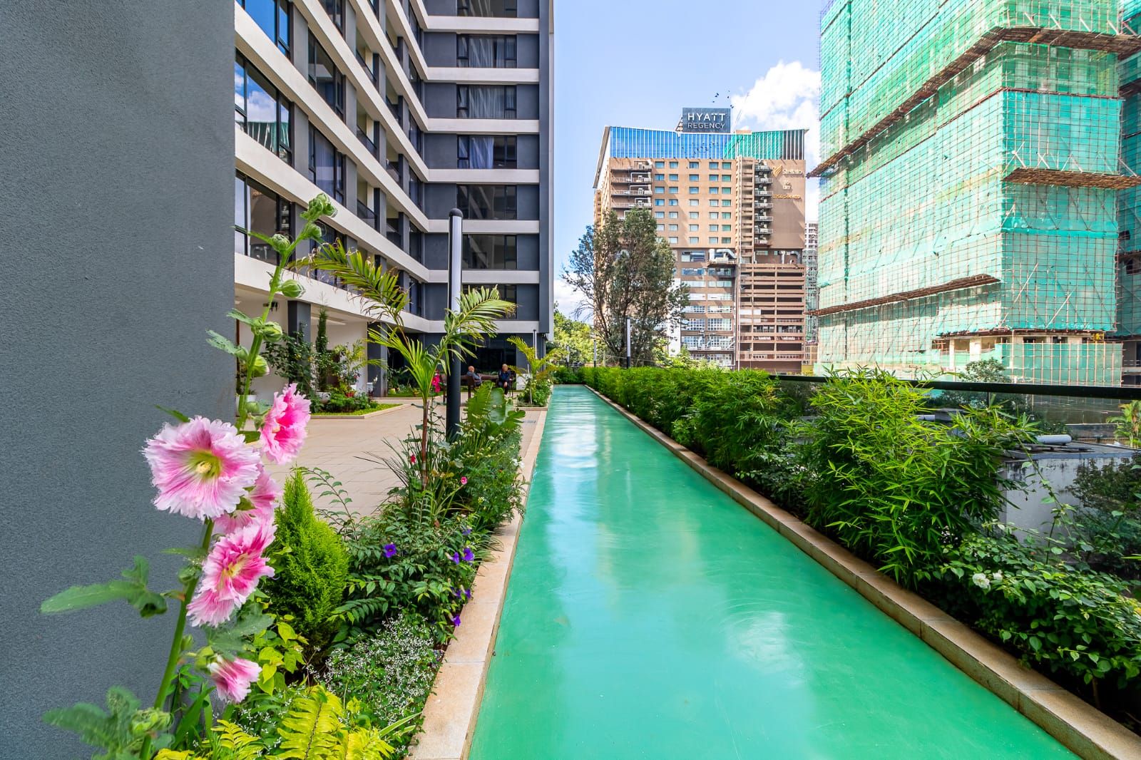 Un edificio moderno con piscina, rodeado de exuberante vegetación y un cielo despejado.