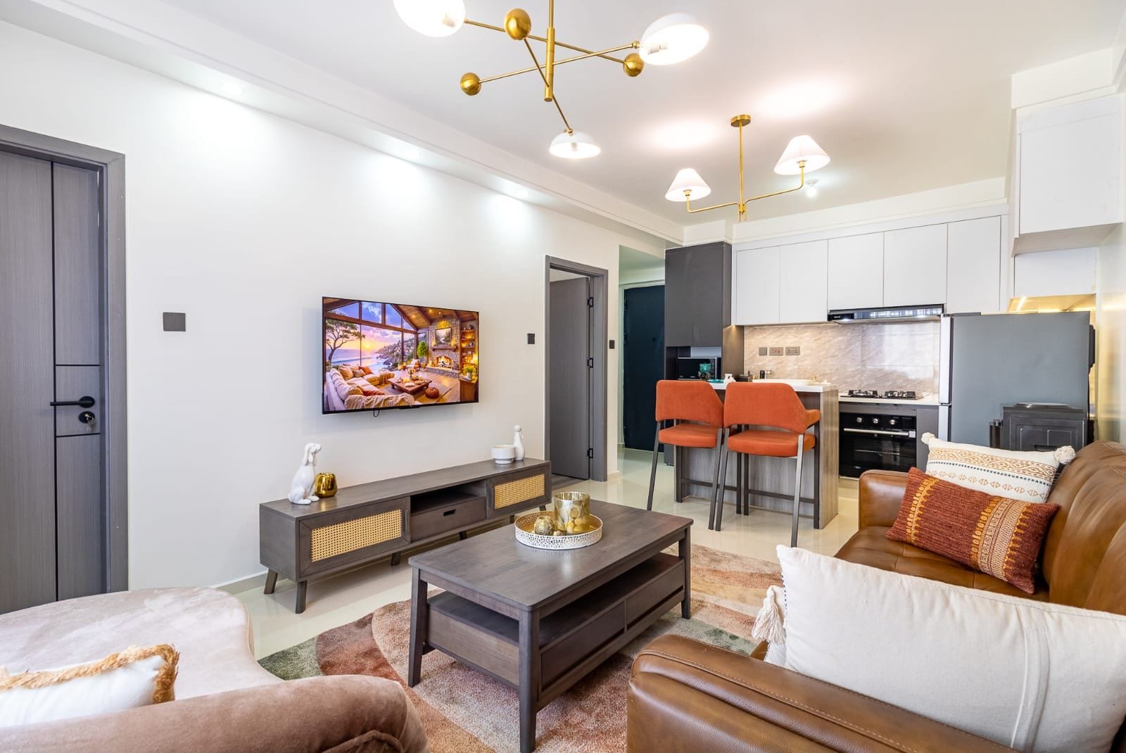 A modern living room with a TV, sofa, coffee table, and a kitchen area with bar stools.