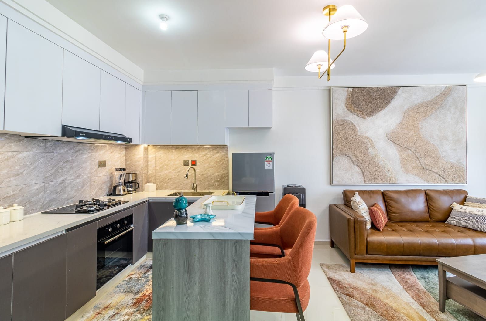 Una cocina moderna con una isla central, un área de comedor con un sofá de cuero marrón y un cuadro abstracto grande en la pared.