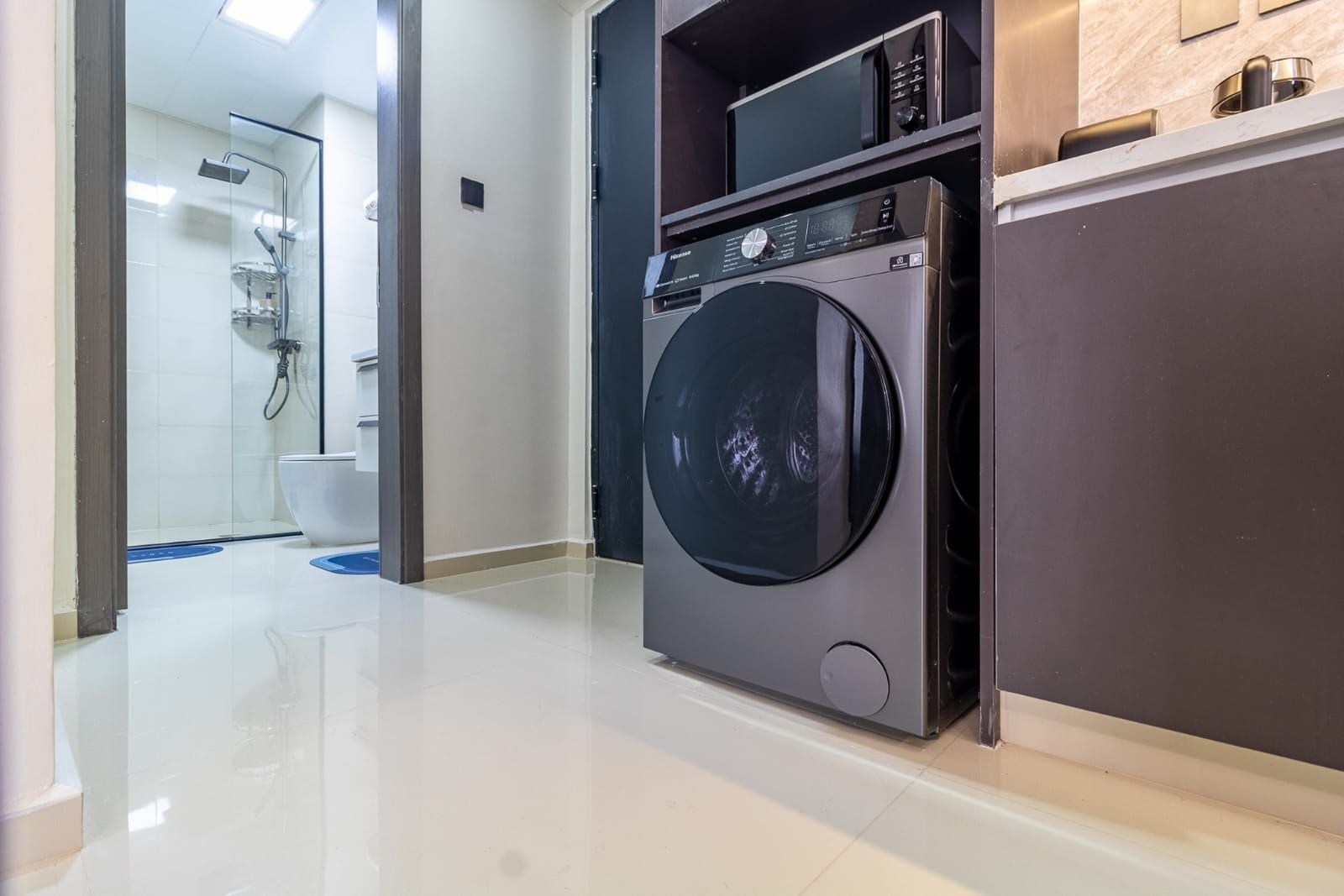 Une cuisine moderne équipée d’un lave-linge et d’un sèche-linge intégrés, d’un four à micro-ondes et d’un plan de travail en acier inoxydable.