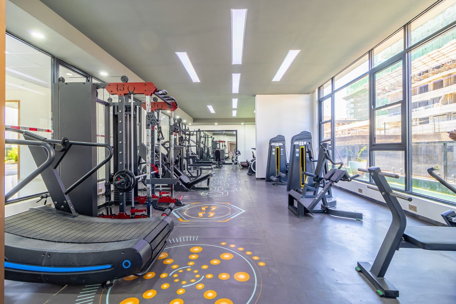 Un gimnasio con máquinas de cardio, equipo de levantamiento de pesas y un amplio ventanal con vistas al exterior.