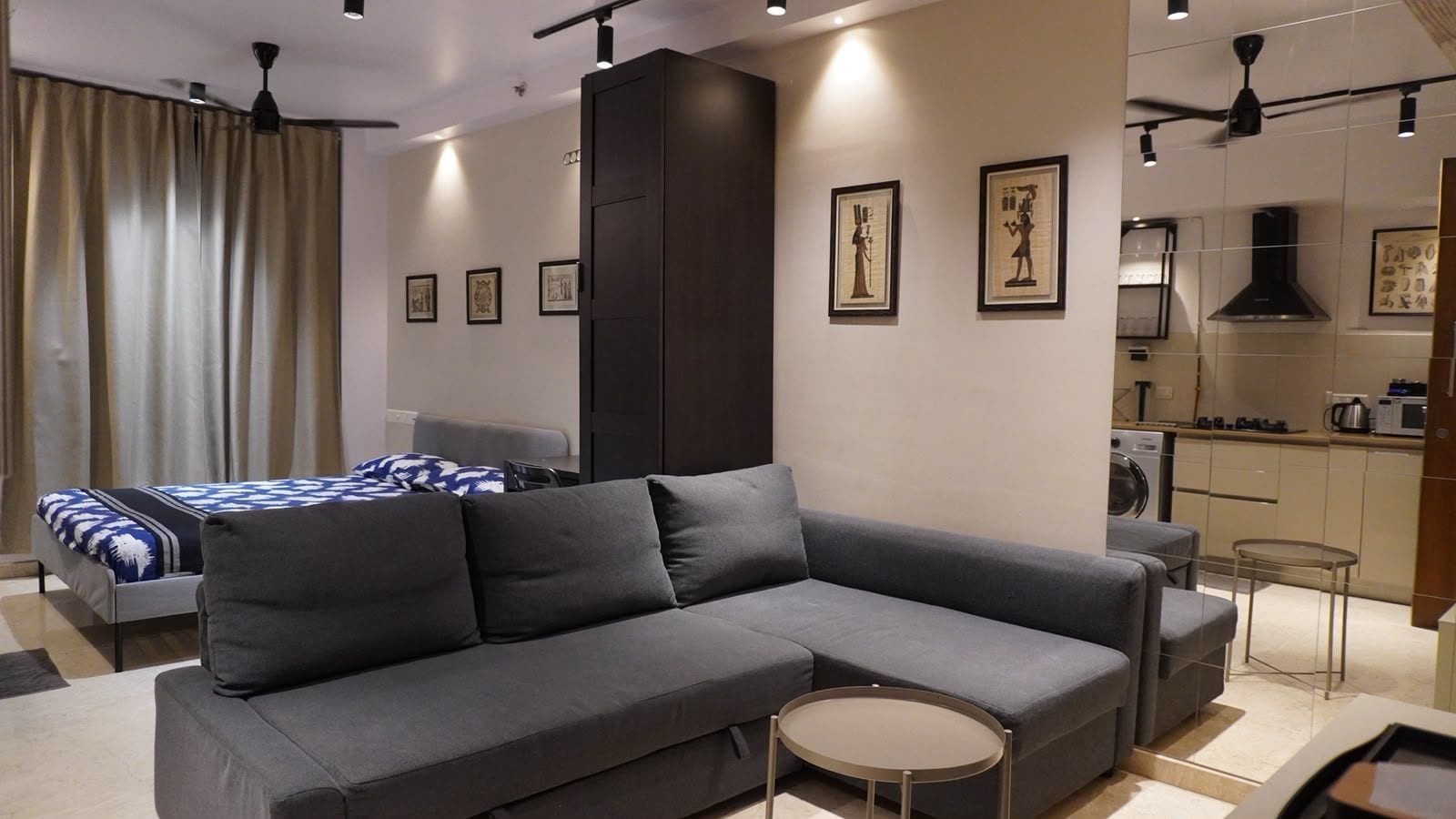 Een moderne woonkamer met een grijze modulaire bank, een klein rond tafeltje en een bed met beddengoed met een patroon.