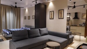 Una sala de estar moderna con un sofá seccional gris, una mesita redonda y una cama con ropa de cama estampada.
