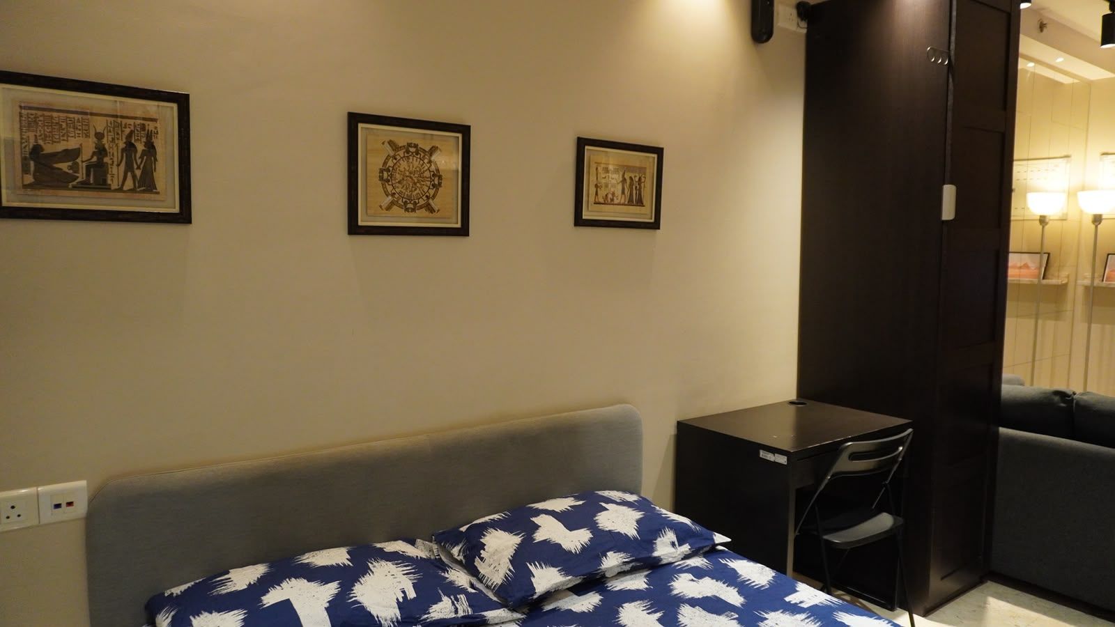 Ein Hotelzimmer mit Bett, Schreibtisch und Kleiderschrank. An der Wand hängen drei gerahmte Bilder.