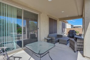 A covered outdoor patio with a glass door leading to a garden, wicker furniture, and a barbecue grill. - Peaceful Home w/ Resort Perks in Buckeye (Buckeye)