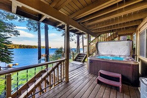 Um deck de madeira com uma banheira de hidromassagem e vista para um lago.